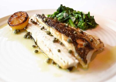 grilled fish on a whit plate with capers, greens and lemon